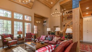 A spacious living room with leather sofas, a fireplace, and large windows offering a view of the outdoors. - Uncle Chris' Cabin (Island Park)