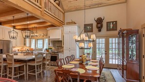 A spacious dining area with a wooden table and chairs, a kitchen with white cabinets, and a large bull head decoration on the wall. - Uncle Chris' Cabin (Island Park)