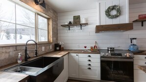 A kitchen with a large window, stainless steel sink, white cabinets, and a built-in oven. - Cast Iron Moose (Island Park)