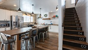 A modern kitchen with a central island, stainless steel appliances, and a wooden staircase. - Cast Iron Moose (Island Park)
