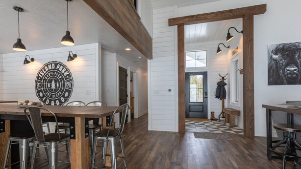 A spacious dining area with a wooden table and metal chairs, a large circular sign on the wall, and a checkered floor pattern. - Cast Iron Moose (Island Park)