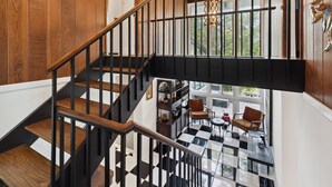 A staircase with wooden steps and black railings leading to a room with a checkered floor, a chandelier, and a view of greenery outside. - Pineview Haven (Knoxville)