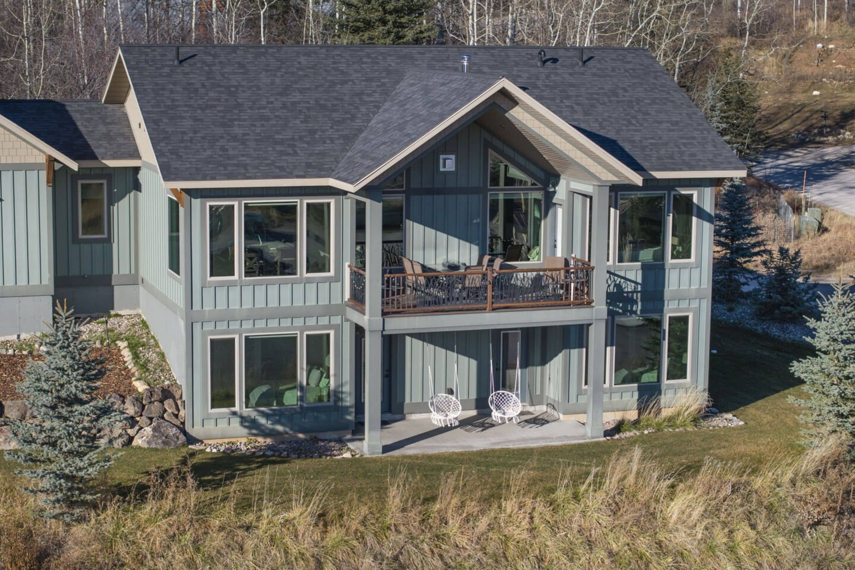 A modern two-story house with a balcony, large windows, and a stone foundation.