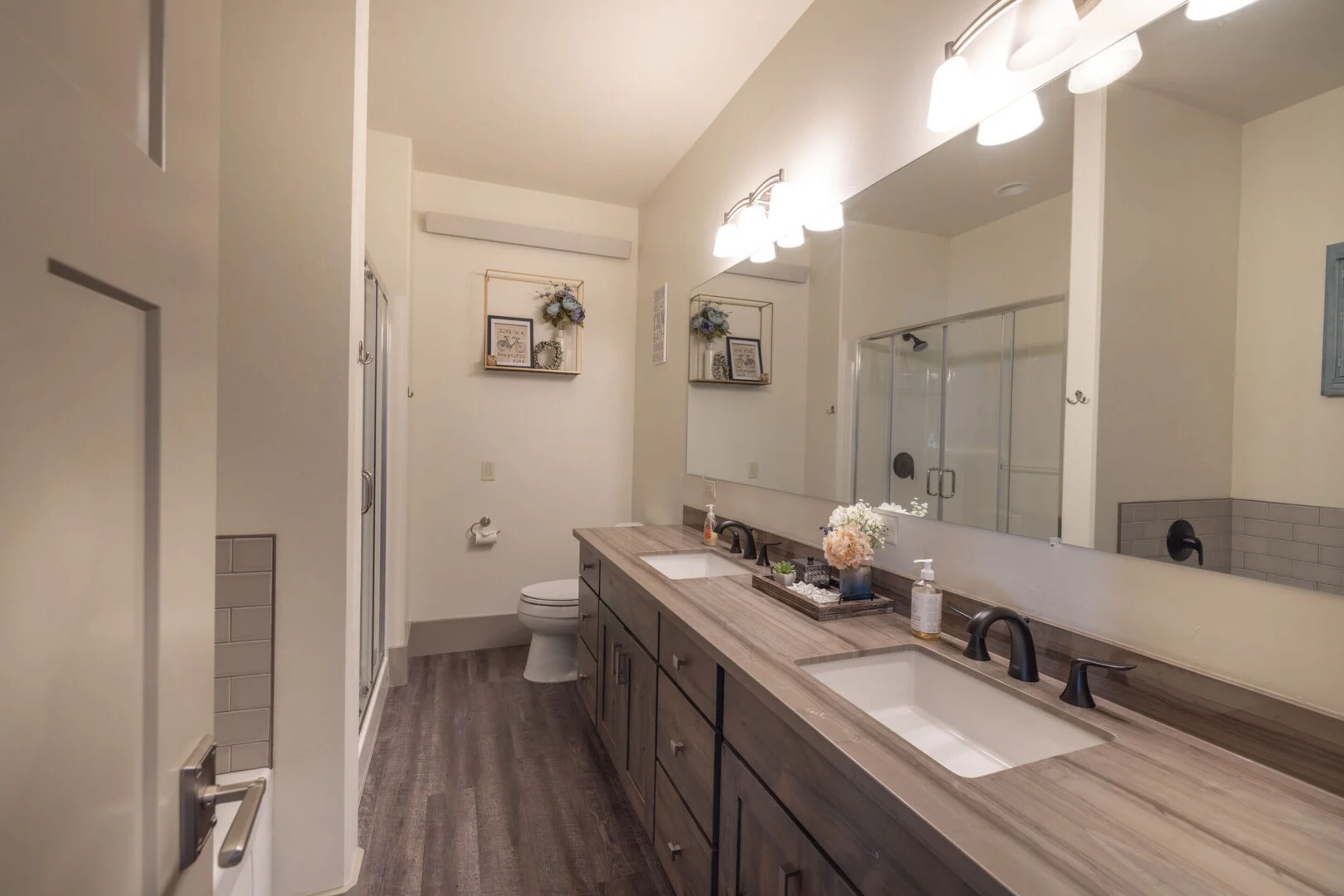 A modern bathroom with a double sink vanity, a large mirror, and a shower.