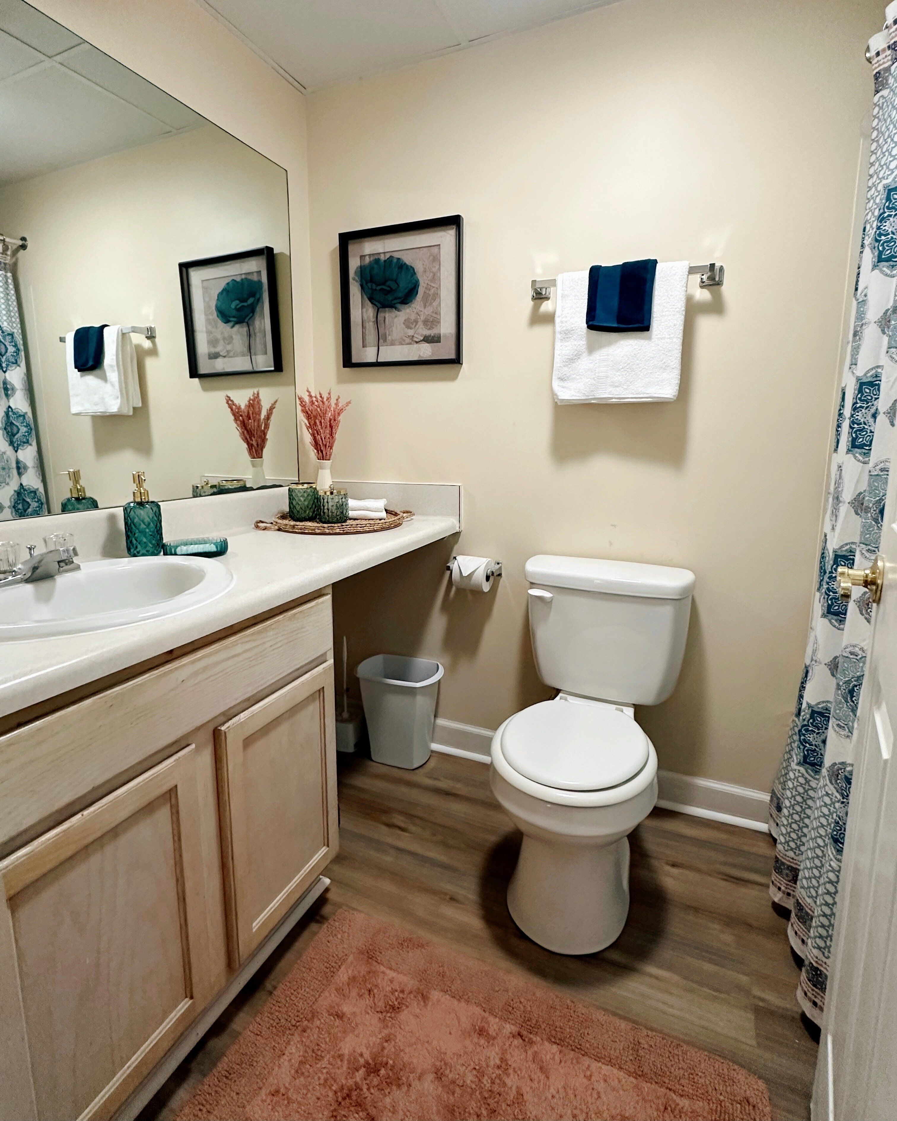 A bathroom with a sink, toilet, and shower curtain. There are towels hanging on the wall and a trash can next to the toilet.