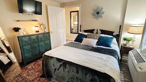 A bedroom with a large bed, a dresser, a TV mounted on the wall, a door, and a decorative wall piece.