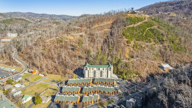 An aerial view of a hotel with multiple buildings, surrounded by a hilly landscape with sparse trees and a clear sky.