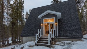 Eine Holzhütte mit dunklen Schindeln, einem weißen Eingangsbereich mit Treppe und einer Veranda.