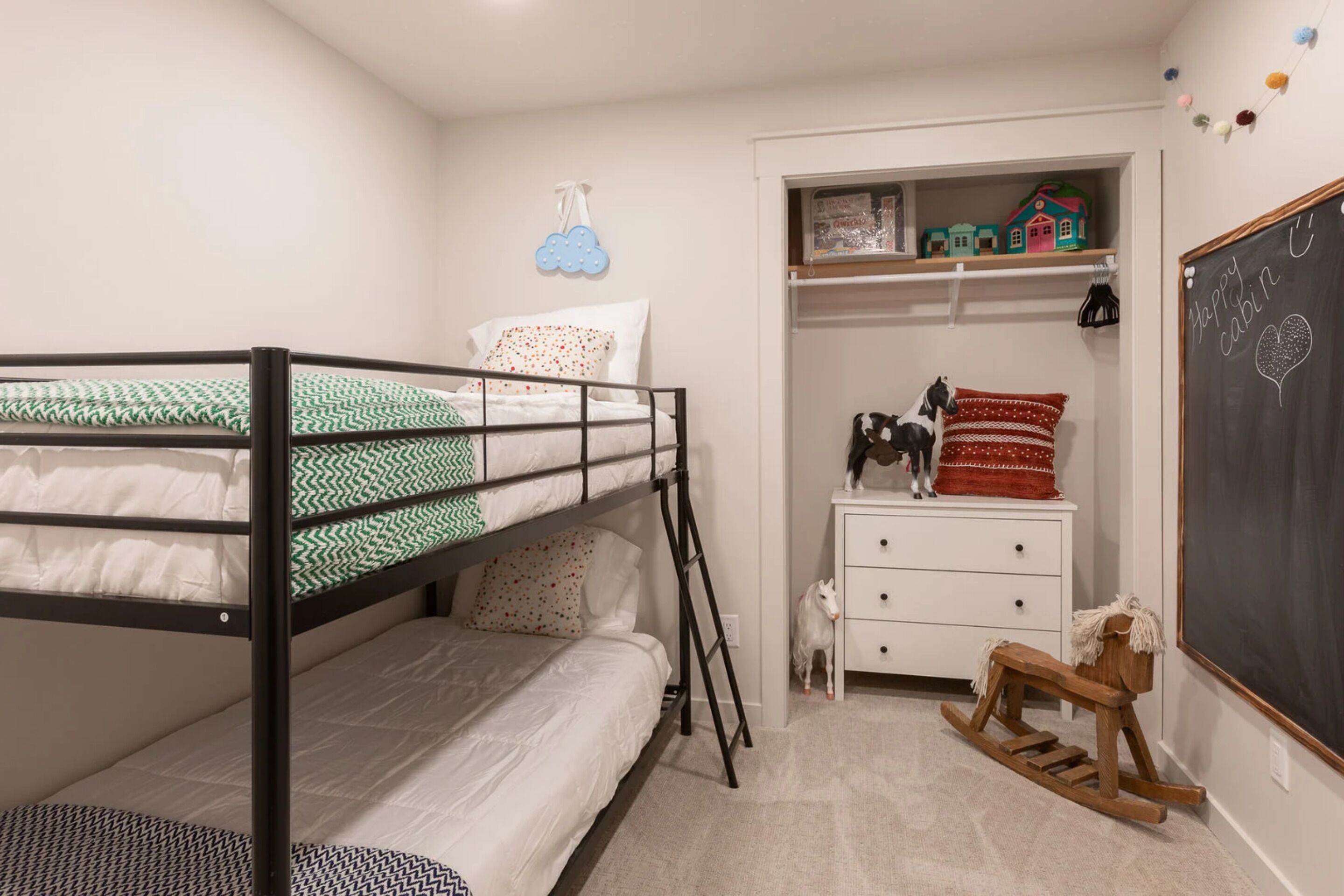 A bunk bed with a ladder, a white dresser with a rocking horse, a small dog, and a chalkboard with "Happy cabin C" written on it.