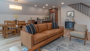 Ein modernes Wohnzimmer mit einer Couch, einem Esstisch mit Stühlen, einer Küchenzeile inklusive Kühlschrank und einer Treppe.