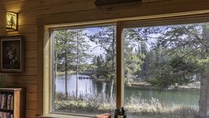 A room with a large window overlooking a lake surrounded by trees. - Buffalo Bliss (Island Park)