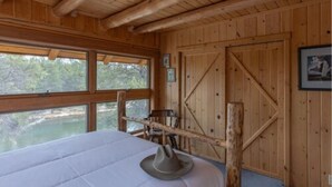 A wooden cabin room with a bed, large windows, and a view of a river. - Buffalo Bliss (Island Park)