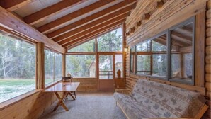 A log cabin with a dining table and a sofa, large windows offering a view of the outdoors. - Buffalo Bliss (Island Park)