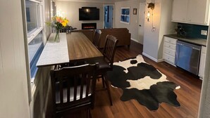 A modern kitchen with a wooden dining table, chairs, a cowhide rug, and a flat-screen TV.