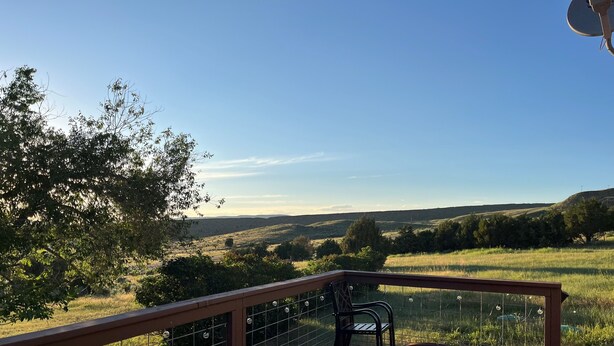 A deck with a metal fire pit, chairs, and a view of a grassy landscape with trees.