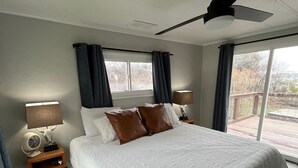A spacious bedroom with a large bed, a ceiling fan, and a view of the outdoors through a sliding glass door.