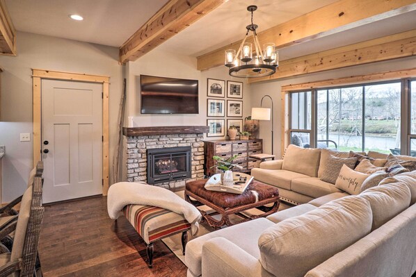 A cozy living room with a fireplace, a large sofa, a coffee table, and a television mounted on the wall.