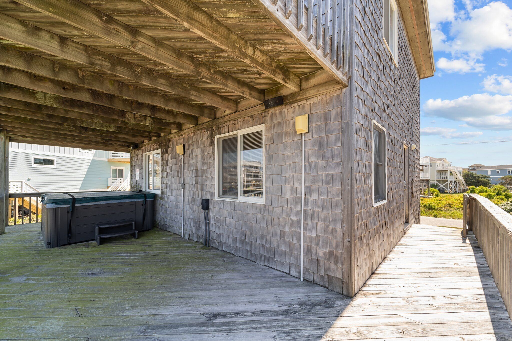 Una terraza techada con un jacuzzi y una terraza de madera que conduce a un edificio con revestimiento de tejas.