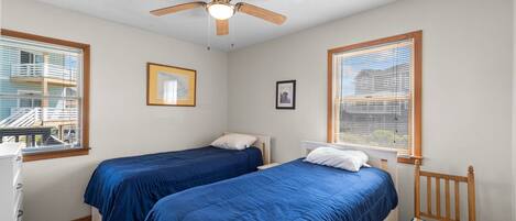 Un dormitorio con dos camas, ventilador de techo y ventanas con persianas.