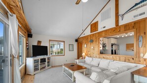 A living room with a white sofa, a wooden coffee table, a TV on a white cabinet, and a large mirror on the wall.