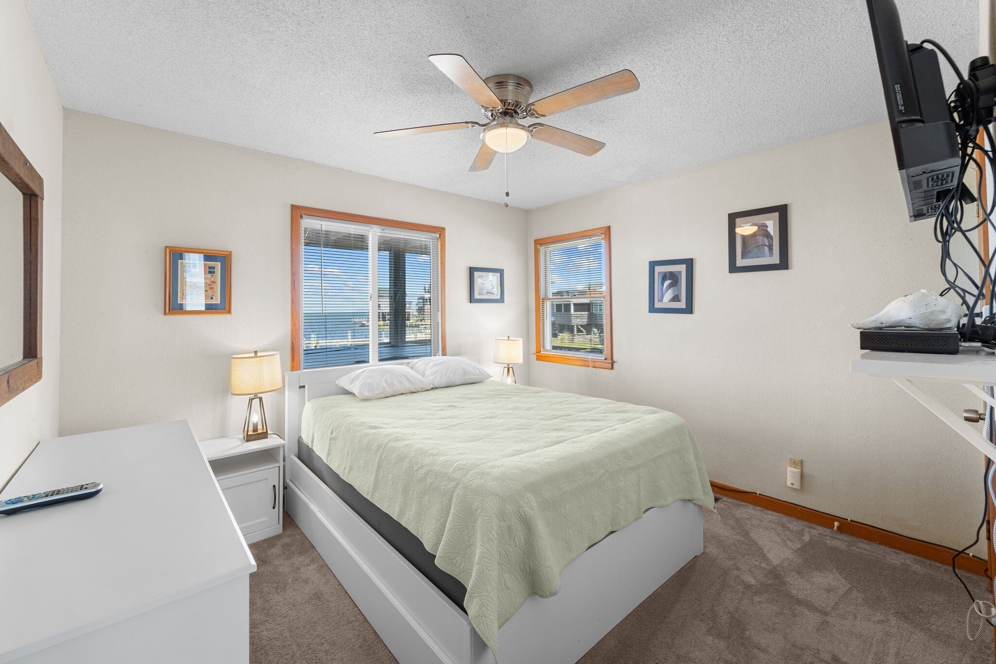 A bedroom with a bed, a desk, a chair, a ceiling fan, and a window with blinds.