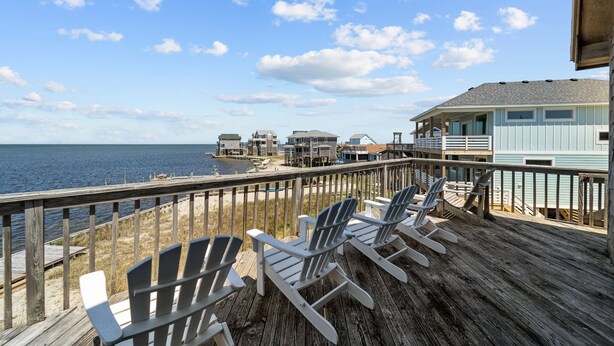 A wooden deck with Adirondack chairs overlooking a beach and ocean.