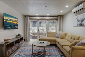 Una sala de estar moderna con un sofá, una mesa de centro, un televisor y un ventanal con cortinas.