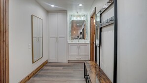 Un pasillo con un banco de madera, armarios blancos y un espejo.