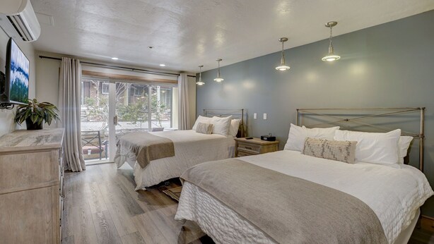 Habitación de hotel con dos camas, un ventanal con cortinas, un ventilador de techo y un televisor en la pared.
