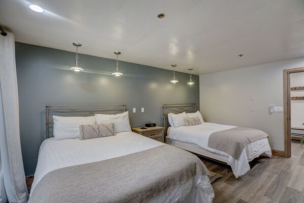 Une chambre d’hôtel avec deux lits, une table de chevet et un luminaire au plafond.