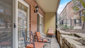 Un balcón con dos sillones de descanso, un muro de piedra y un edificio de ladrillo con una puerta de cristal.