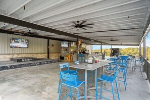 An outdoor patio area with blue chairs and tables, a bar counter, and a television screen displaying sports.