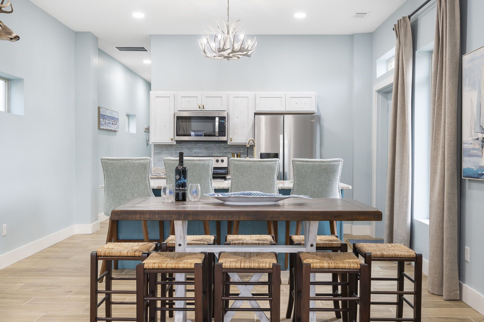 Une cuisine moderne avec des meubles blancs, des appareils en acier inoxydable et un coin repas comprenant une table en bois et des chaises en osier.