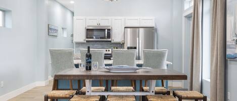 Una cocina moderna con armarios blancos, electrodomésticos de acero inoxidable y un comedor con mesa de madera y sillas de mimbre.