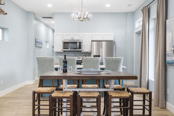 A modern kitchen with white cabinets, stainless steel appliances, and a dining area with a wooden table and wicker chairs.