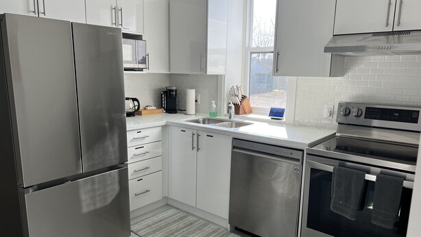 A modern kitchen with stainless steel appliances, white cabinetry, and a window providing natural light. - The Merlot, minutes to Niagara's Falls, 3 bedrooms with Hottub and Sauna (Niagara Falls)