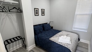 A bedroom with a bed, a bench, a patterned rug, and a window with blinds. - The Merlot, minutes to Niagara's Falls, 3 bedrooms with Hottub and Sauna (Niagara Falls)