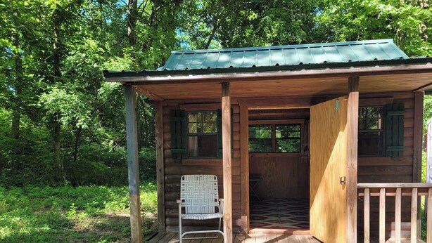 Una cabaña de madera con un porche, una silla y una puerta de entrada.