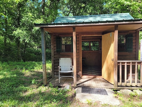 A wooden cabin with a porch, a chair, and a door leading inside.. Celtic Glen Farm Stay - Mini Log Cabin
