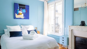 Una camera d'hotel con un letto grande, una parete blu, una finestra con vista sulla strada, un camino e un quadro appeso al muro.