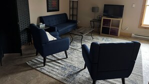 Een woonkamer met een bank, fauteuils, een salontafel, een televisie en een plafondventilator.
