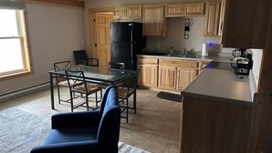 Een moderne keuken met houten kasten, een zwarte koelkast en een eethoek met een glazen tafel en stoelen.