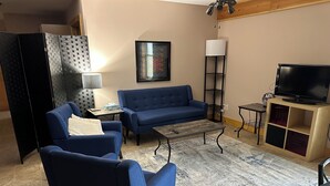 Een woonkamer met een blauwe bank, een salontafel, een televisie op een houten kast en een vloerlamp.