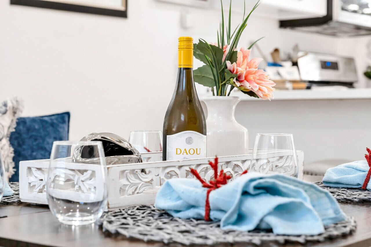 Una mesa con una botella de vino, copas y un florero decorativo con flores.