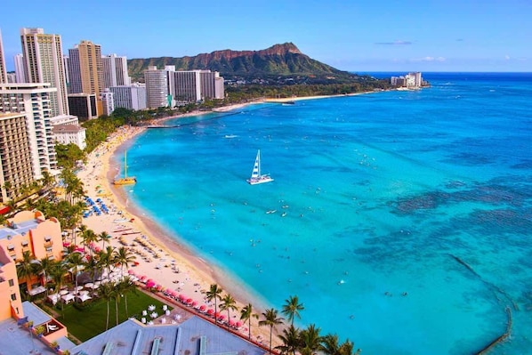 A coastal cityscape with a beach, high-rise buildings, and a sailboat in the water.