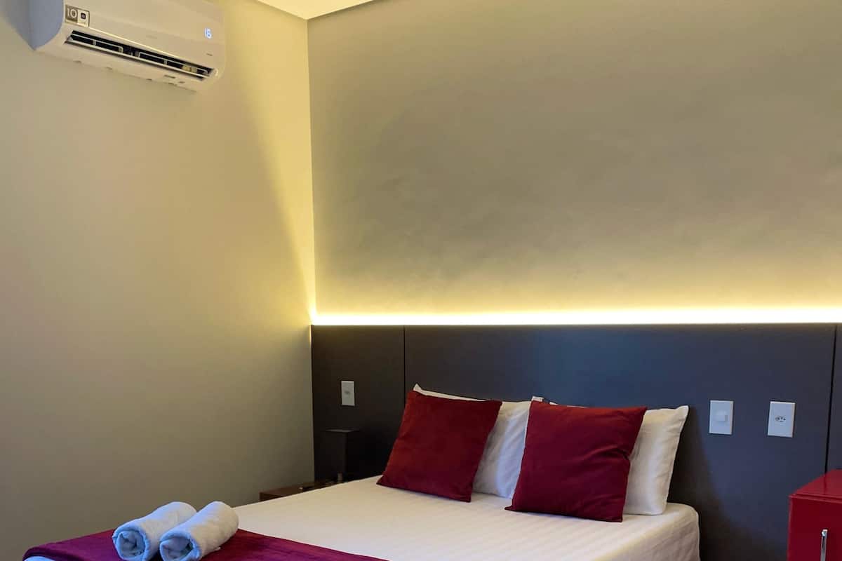 Una habitación de hotel con una cama, un armario rojo y un equipo de aire acondicionado.