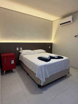 A hotel room with a bed, a red minibar, and an air conditioning unit. - Cubo Hotel (Rio Branco)