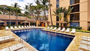 Une piscine avec des chaises longues, des palmiers et un bâtiment doté de nombreuses fenêtres.