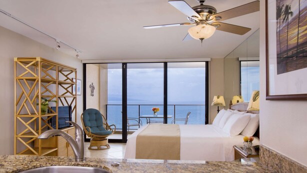 Une chambre d’hôtel moderne dotée d’un balcon, d’un lit, d’un coin salon et d’une cuisine avec un évier.