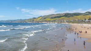 Una playa con gente, olas y colinas al fondo.